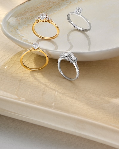 Image of engagement rings in a bowl and table background. Tap to shop all engagement rings image